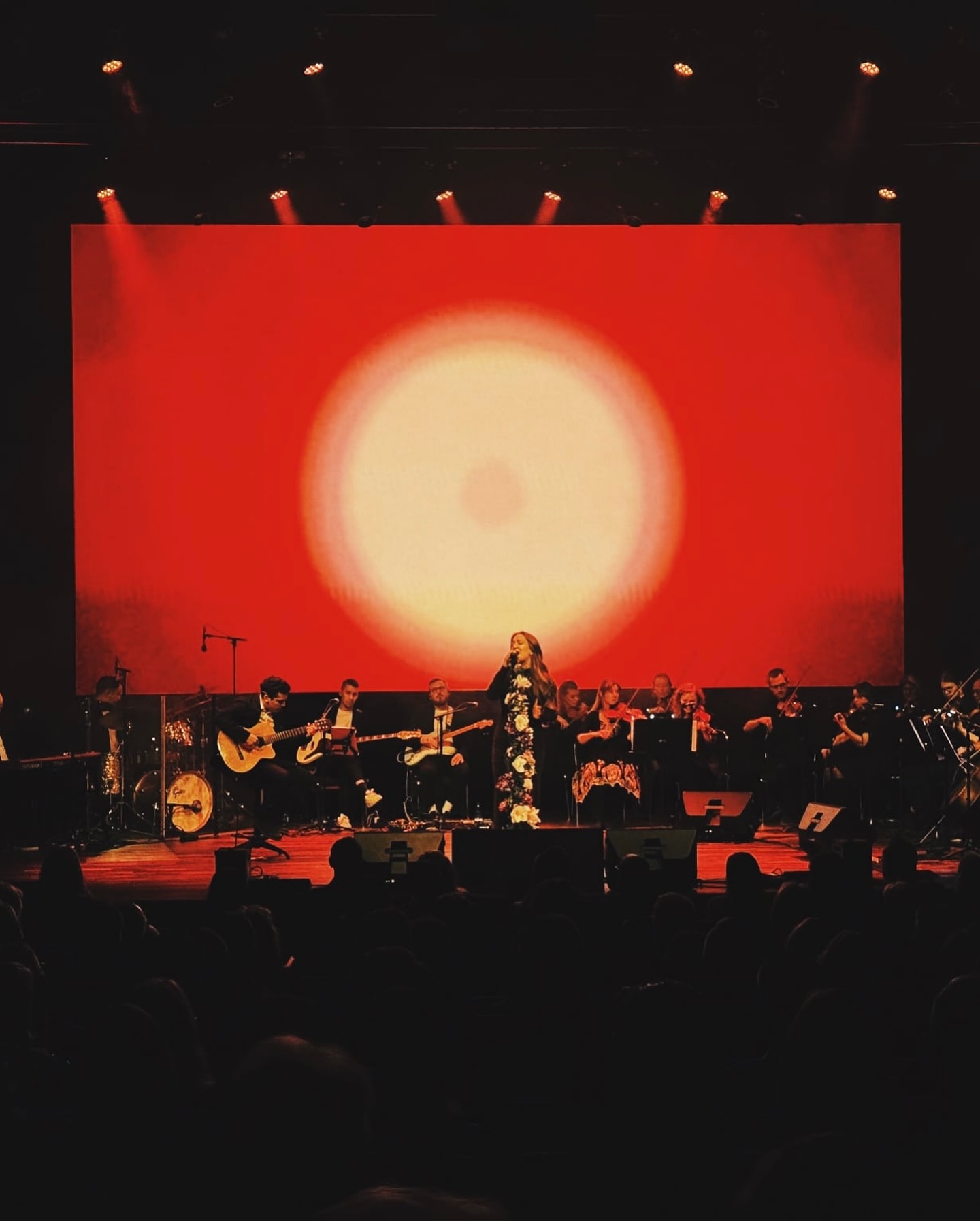 Olsson Estrada performing with a string orchestra beneath a red sunset projection.